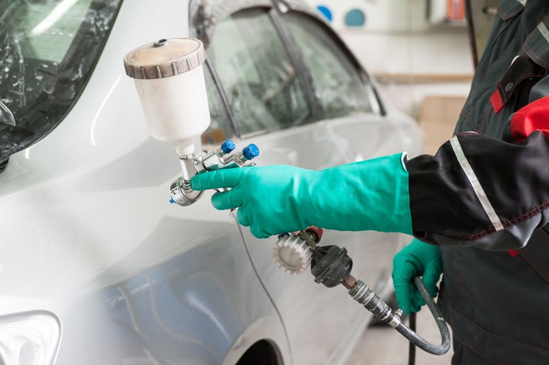Painter applying paint to a car panel with a spray gun